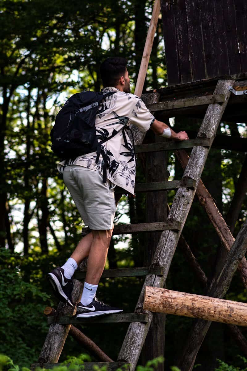 Man climbing a wooden ladder in the forest with a backpack