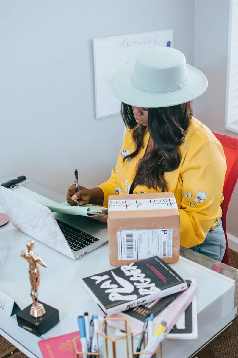 Woman in a yellow jacket and white cowboy hat working at a laptop in a creative workspace